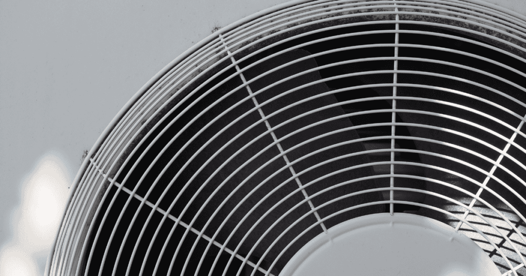 Close-Up View Of A Metallic Fan With A Circular Grille. The Fan Blades Are Visible Through The Gaps. The Image Is Predominantly Black And White With A Minimalistic Design.